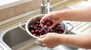 Mani che lavano ciliegie sotto l'acqua corrente in un colino da cucina