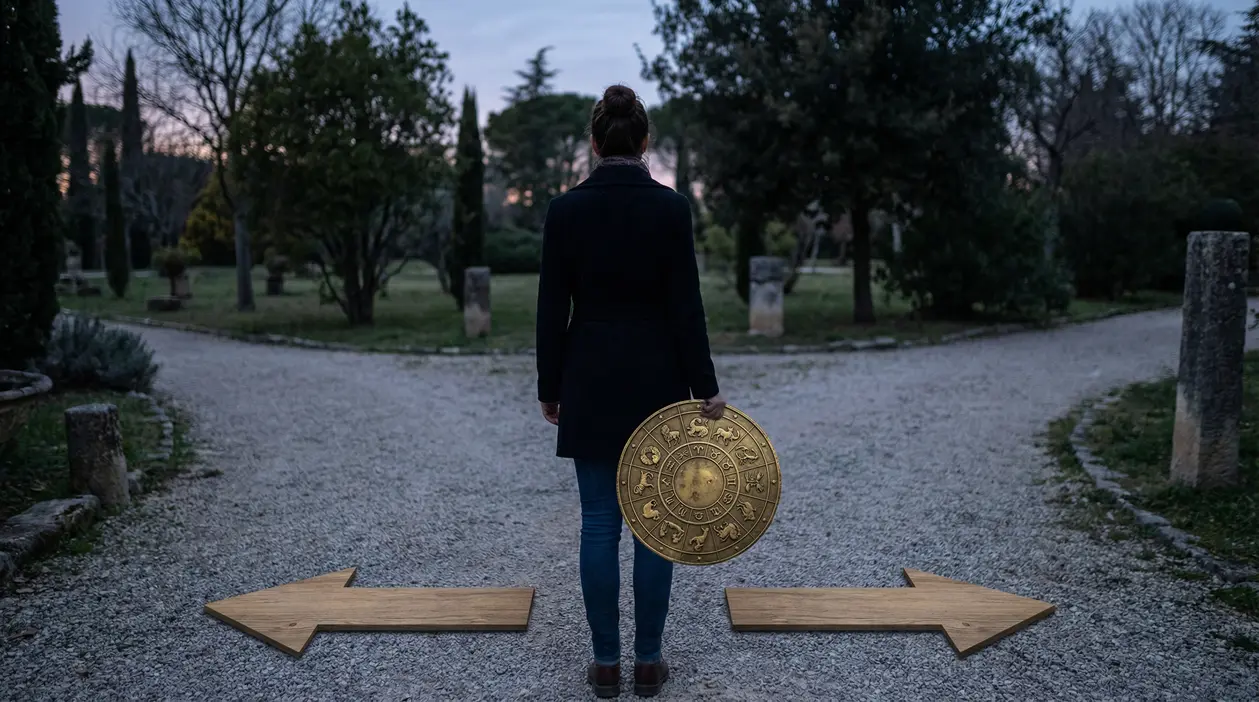 Persona di spalle su un bivio con in mano un disco zodiacale