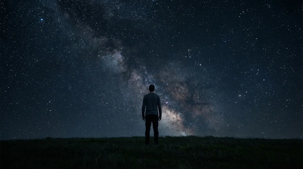 Persona osserva il cielo stellato durante la notte da un campo buio